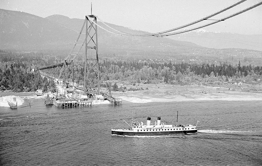 A small Union Steamship is passing under the Lions Gate Bridge during its construction. This view gives us a glimpse of North Vancouver which still appears almost entirely forested. 